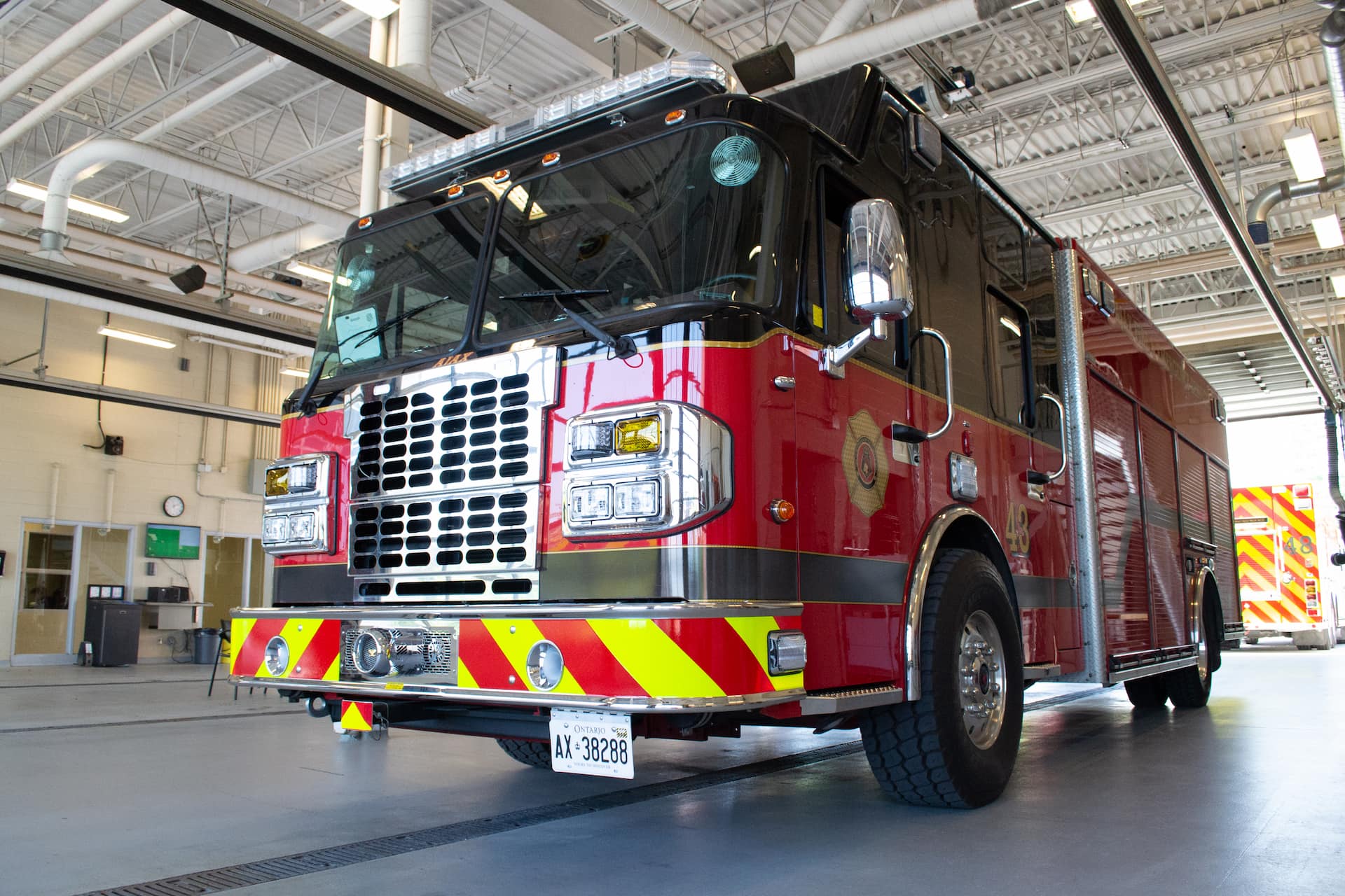 Red fire engine parked inside a fire station garage with its lights off and garage door open.
