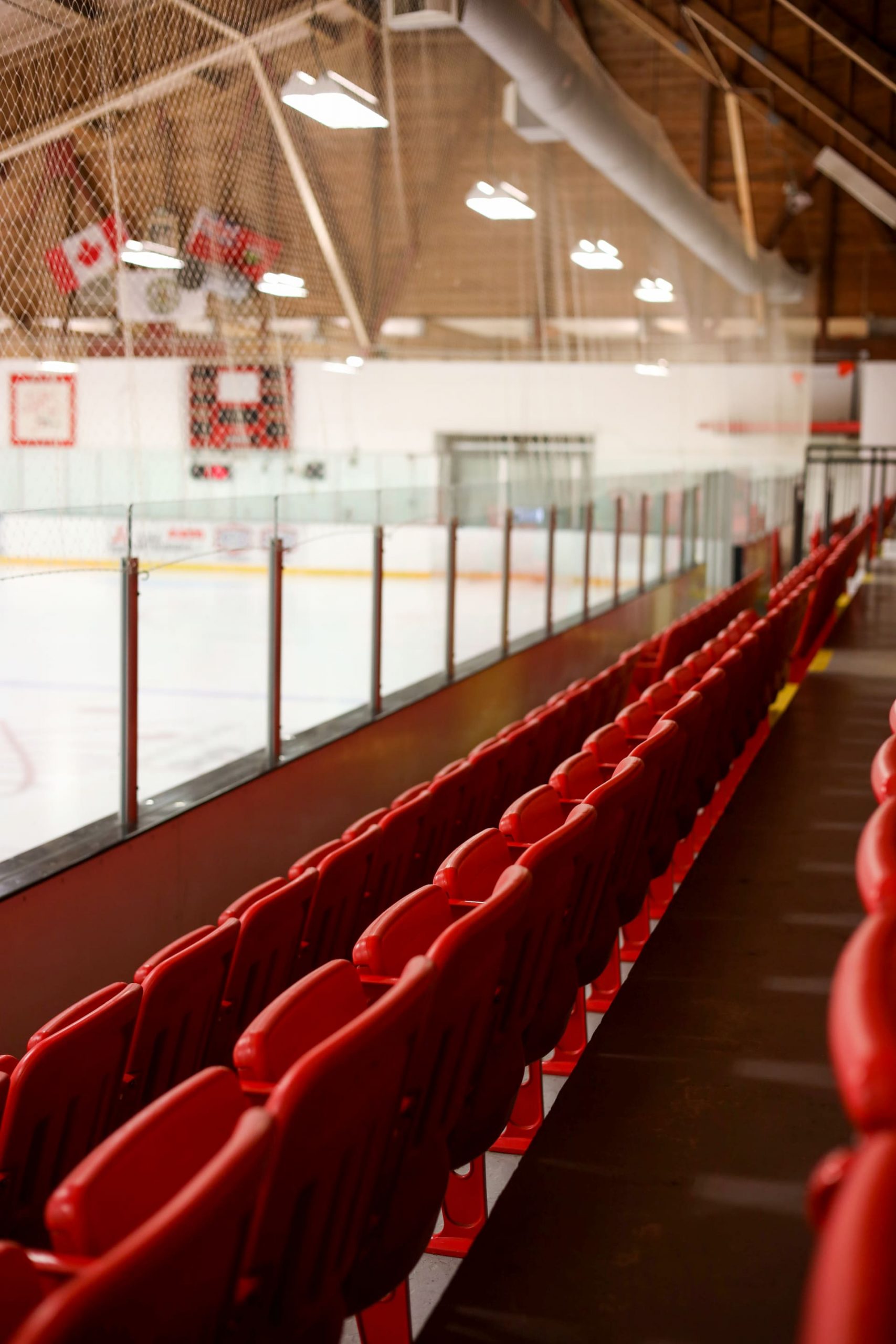Rows of empty red seats in an indoor ice hockey arena with the rink and Canadian flags visible in the background.