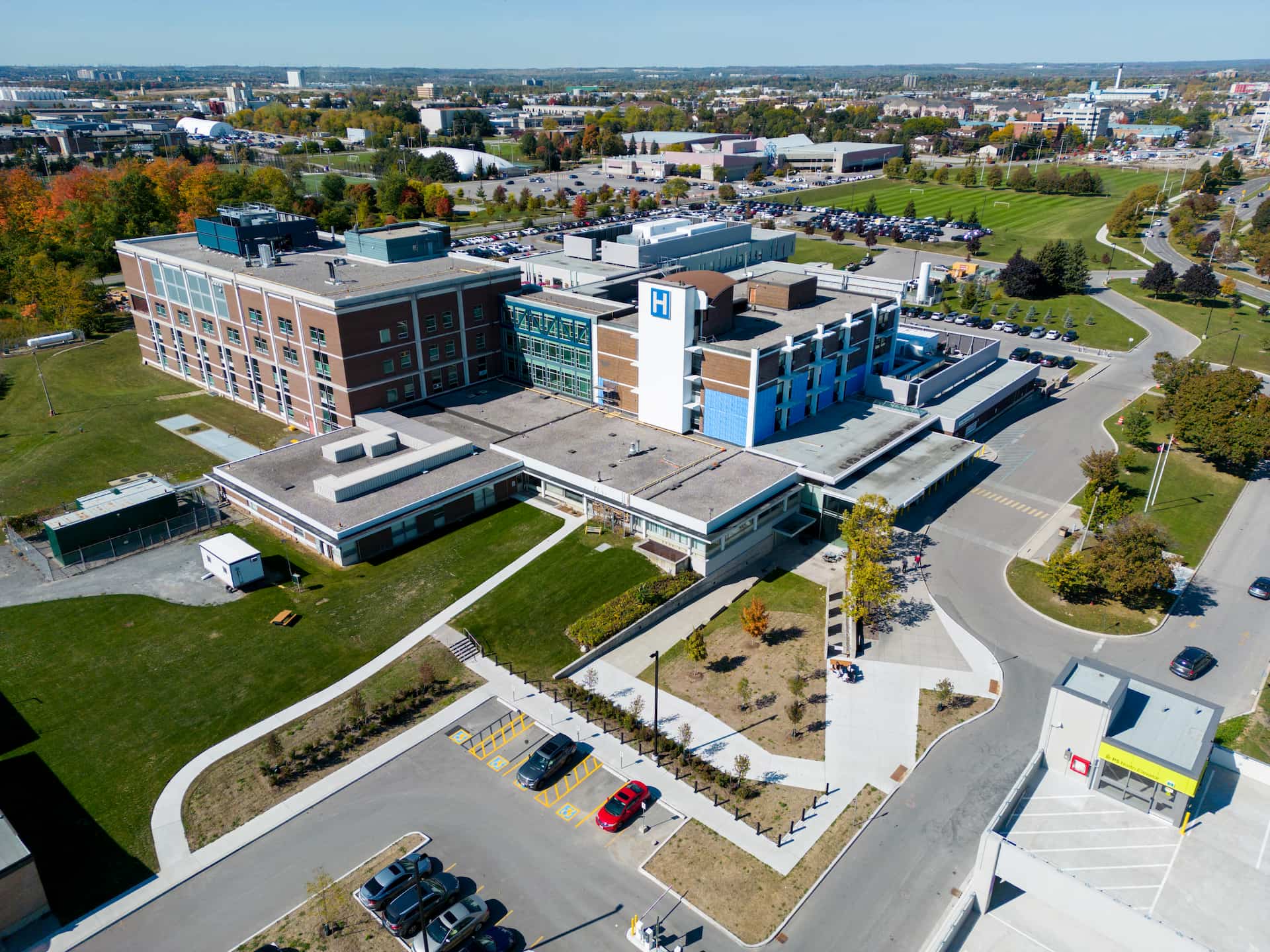 Aerial view of a large hospital complex with adjacent car parks and surrounding green spaces on a clear day.
