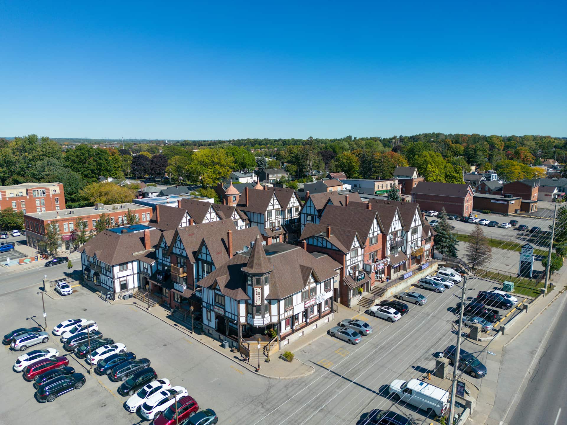 Aerial view of Tudor-style buildings surrounded by parked cars in a small town on a clear, sunny day.
