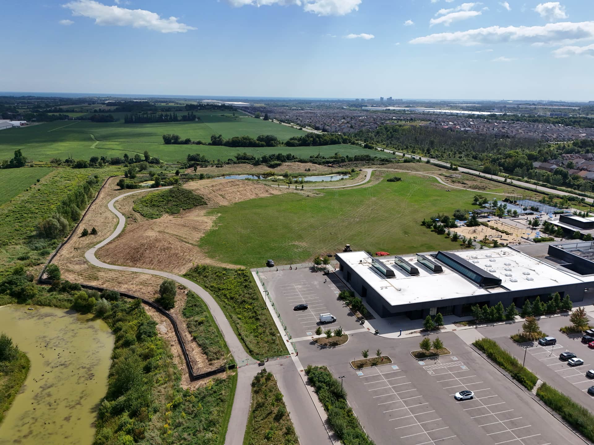 Aerial view of a large grassy park with walking paths, adjacent to a car park and commercial building.