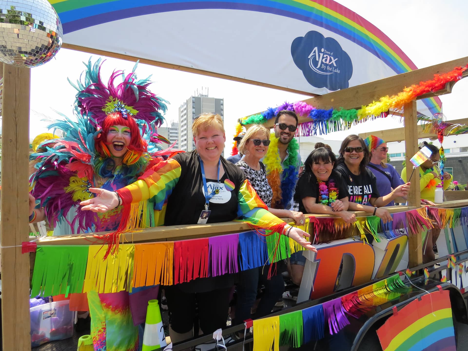 A group of people in colourful rainbow outfits on a parade float decorated with rainbow streamers and a disco ball.