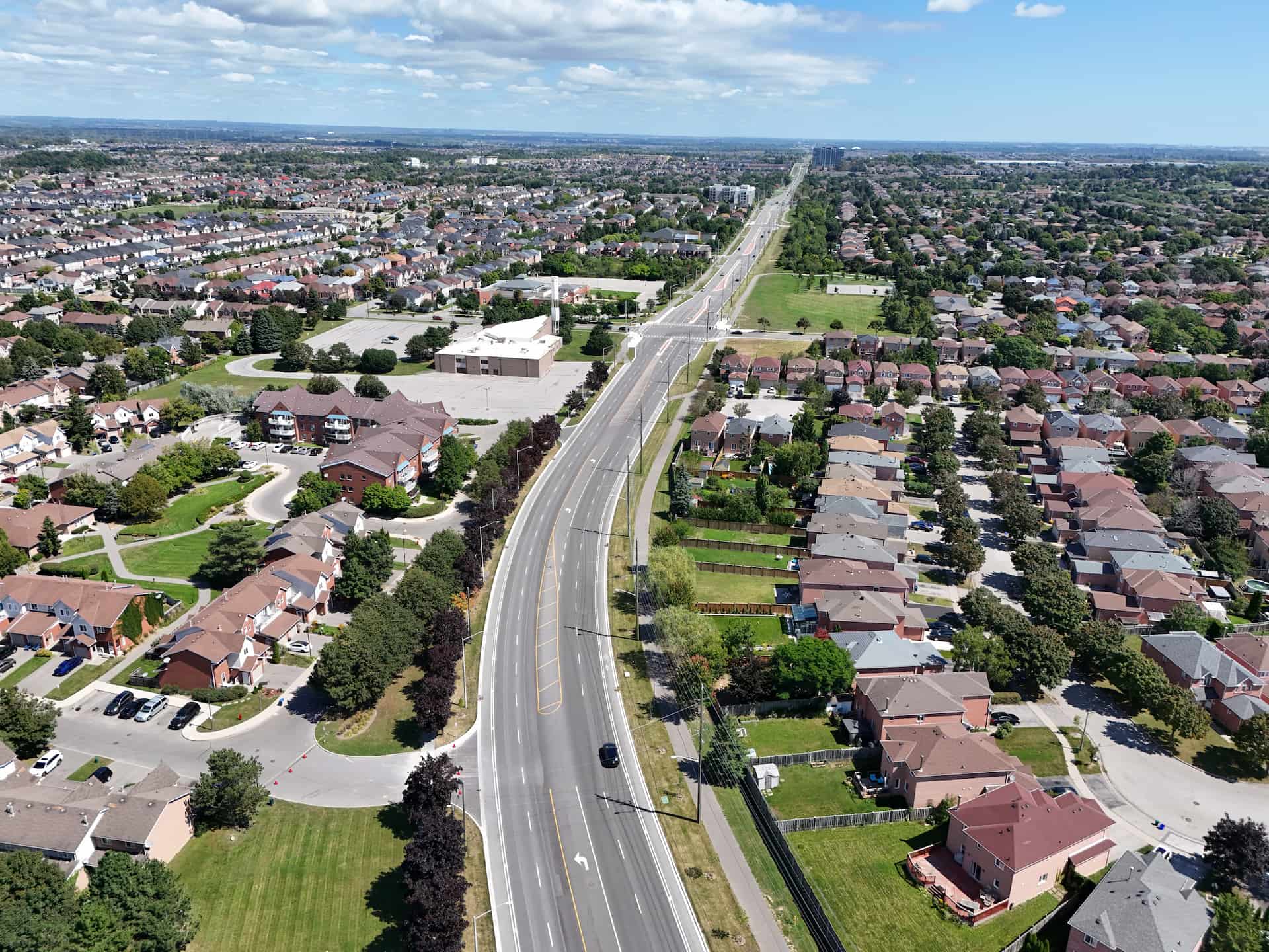 Aerial view of a suburban neighbourhood with houses, roads, and green spaces under a partly cloudy sky.