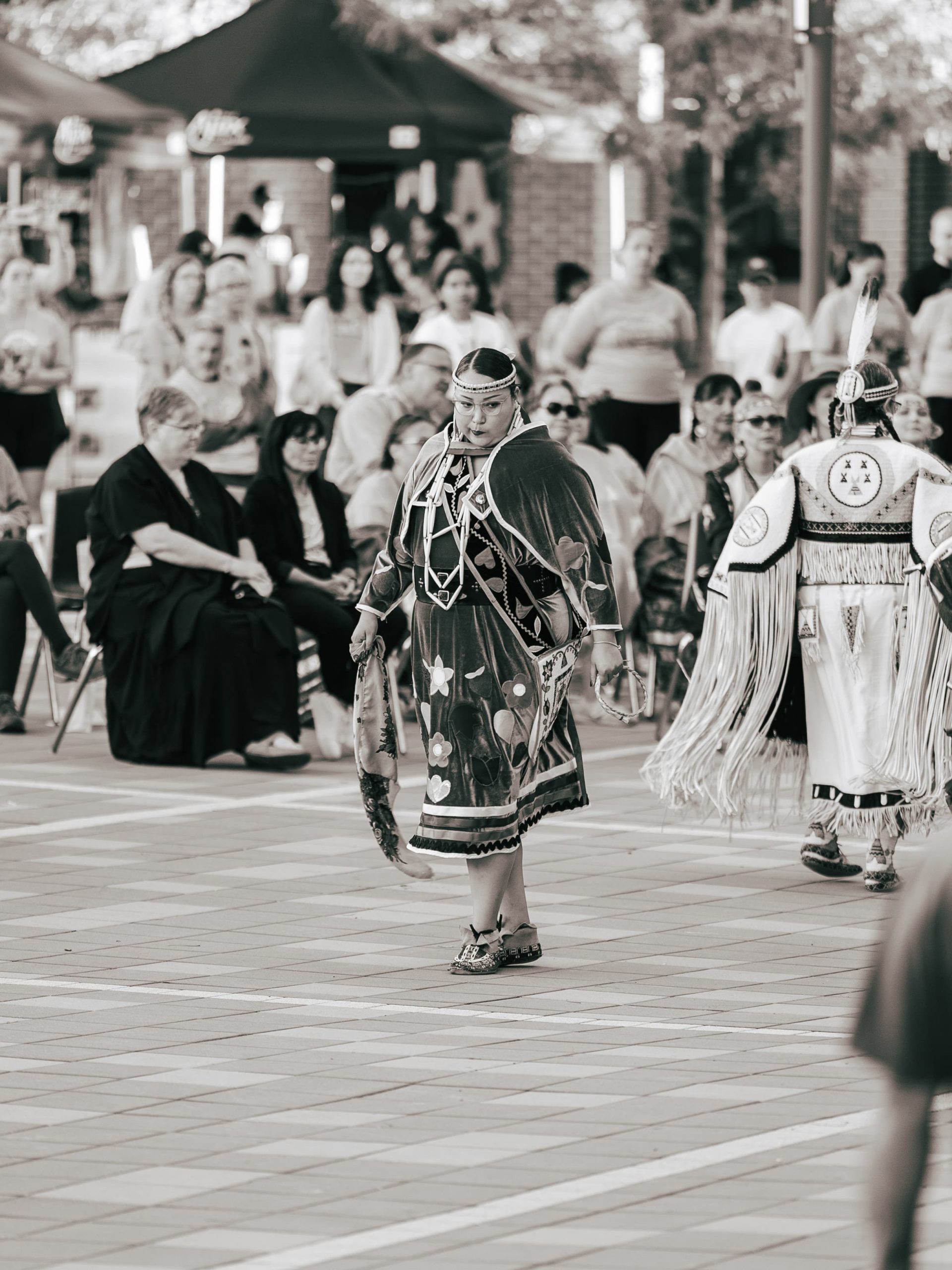 A person in traditional attire dances outdoors in front of a seated audience at a cultural event.