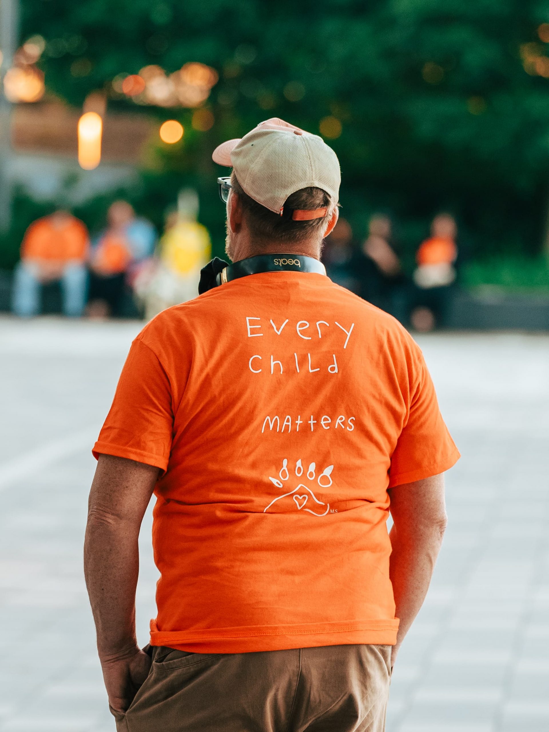 Person wearing an orange shirt with "Every Child Matters" printed on the back, standing outdoors.