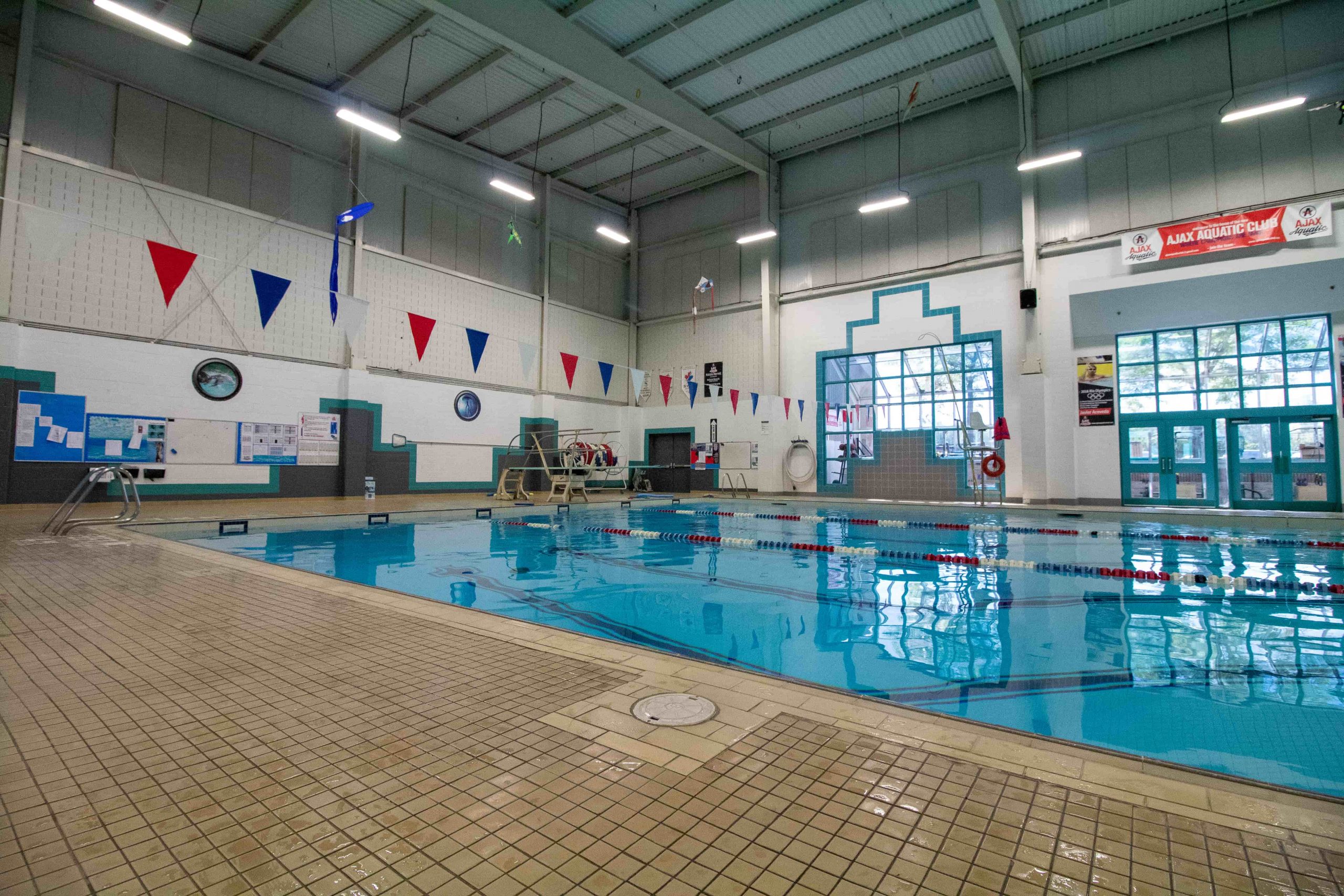 Indoor swimming pool with lane dividers, lifeguard's chair, tiled floor, and flags hanging overhead.