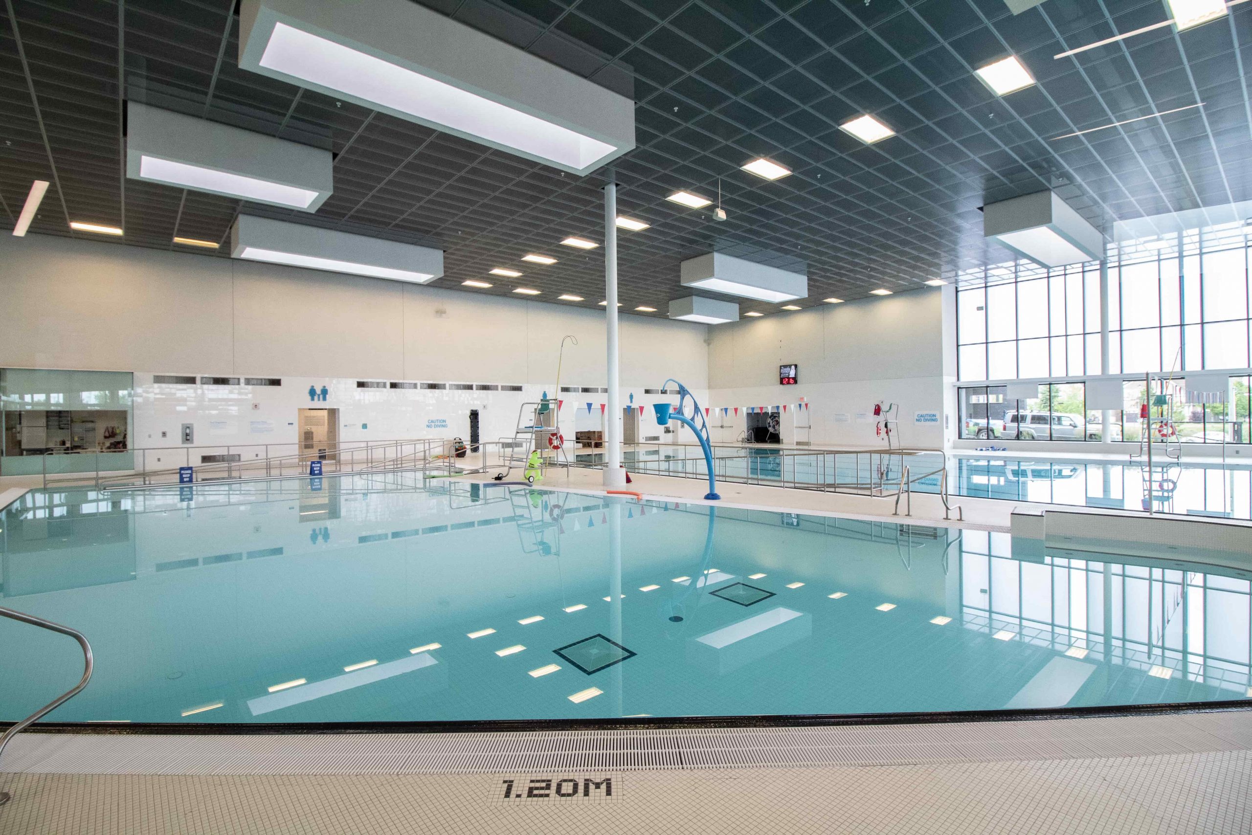 Indoor swimming pool with clear water, accessibility equipment, lane dividers, and large windows letting in natural light.