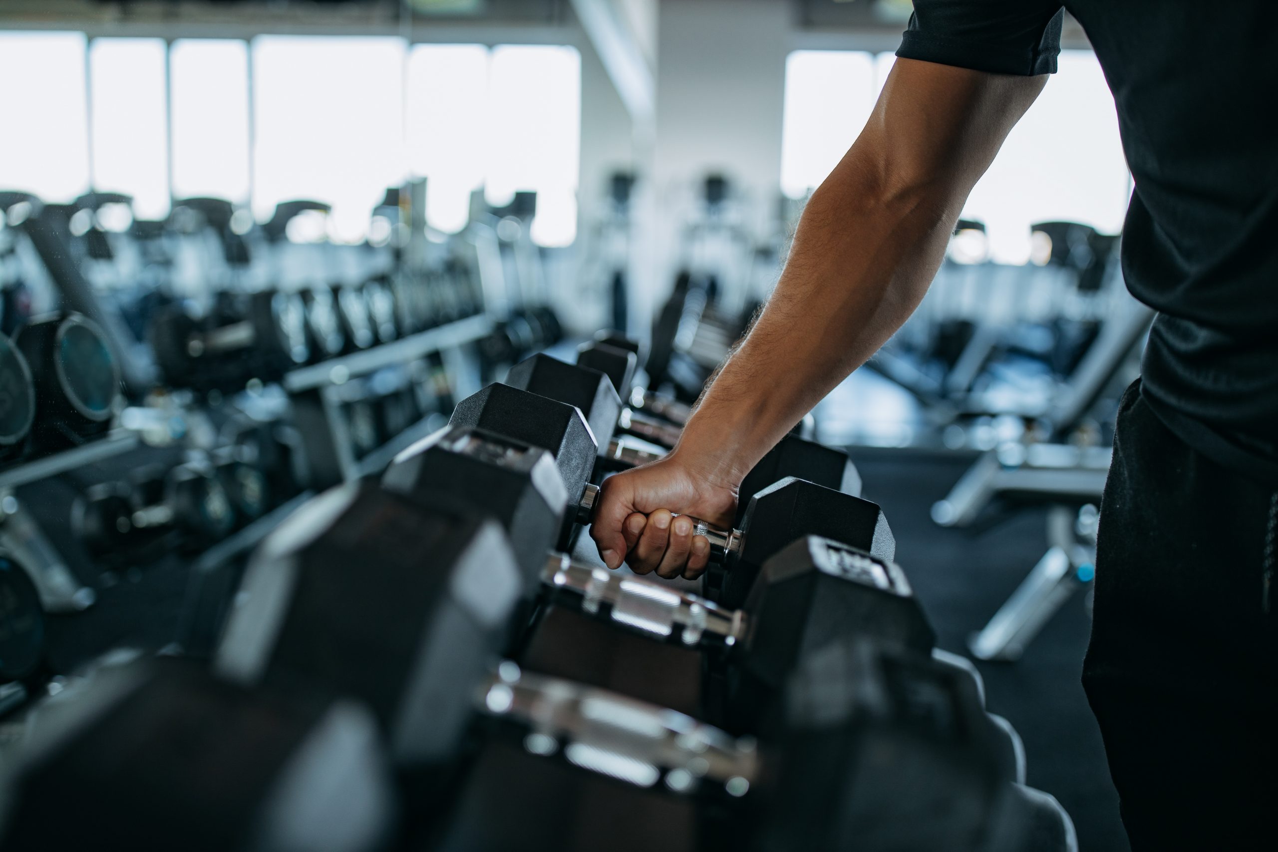 Person picking up a dumbbell from a rack in a gym with various weights in the background.