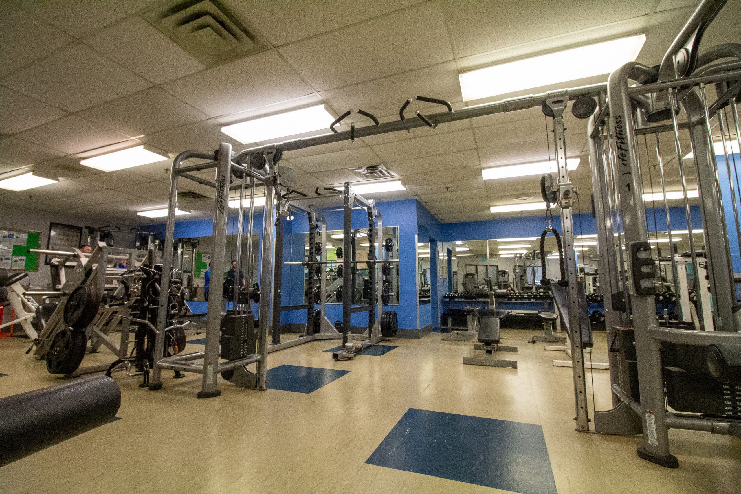 A gym with weight machines, cable equipment, benches, and mirrors in a well-lit room with blue accents.