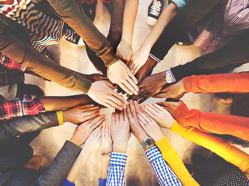 A group of people standing in a circle place their hands together in the centre, photographed from above.