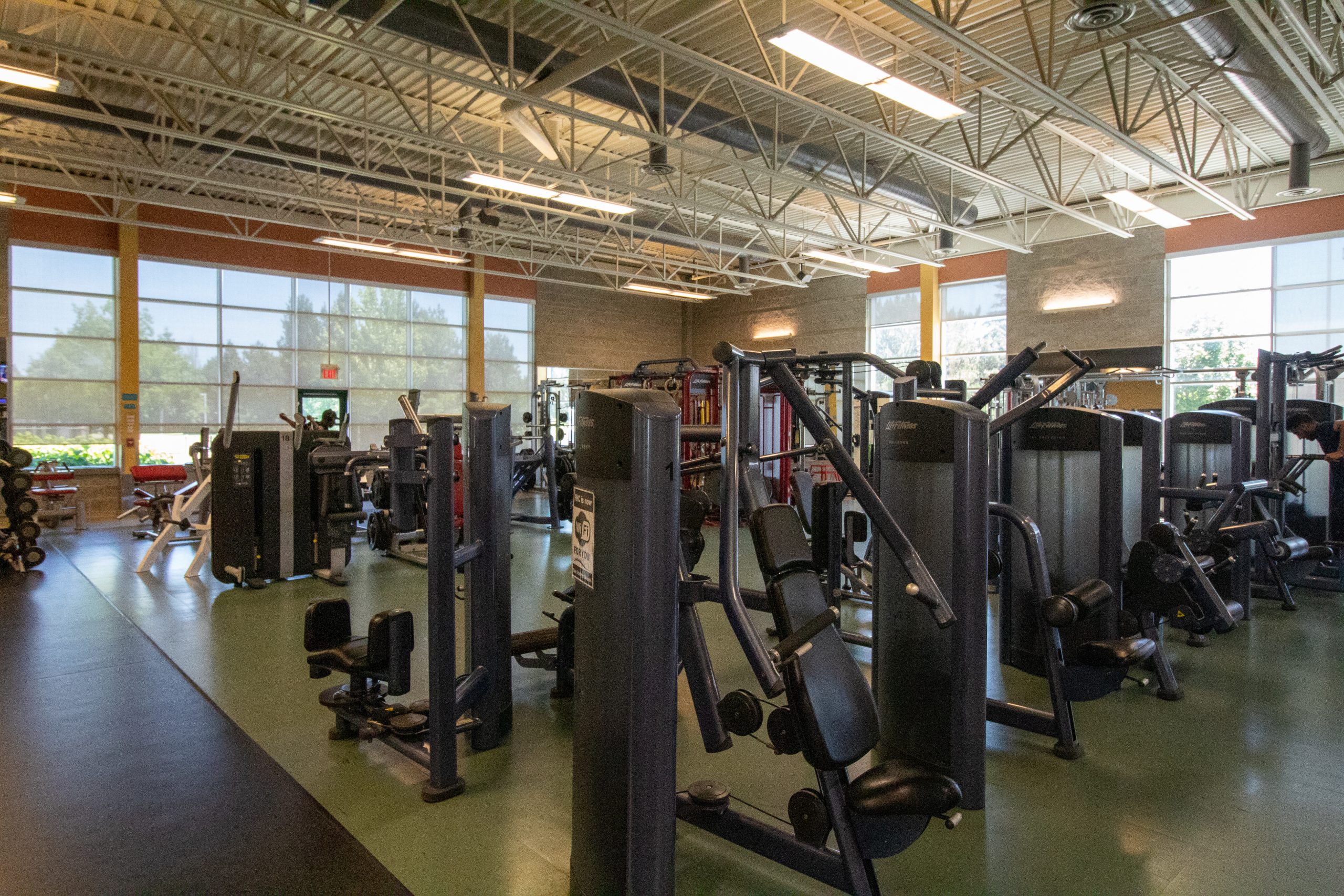A spacious gym with various weight machines, cardio equipment, and large windows letting in natural light.