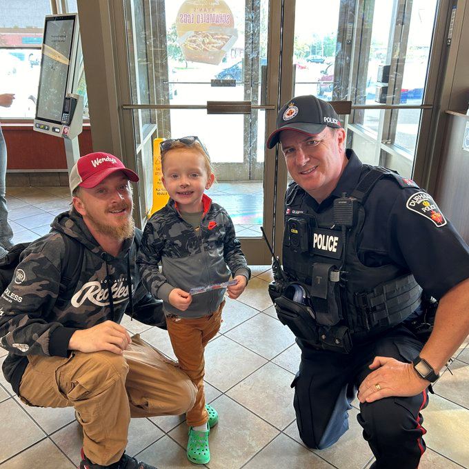 A police officer poses with a smiling child and an adult inside a fast food restaurant near the entrance.